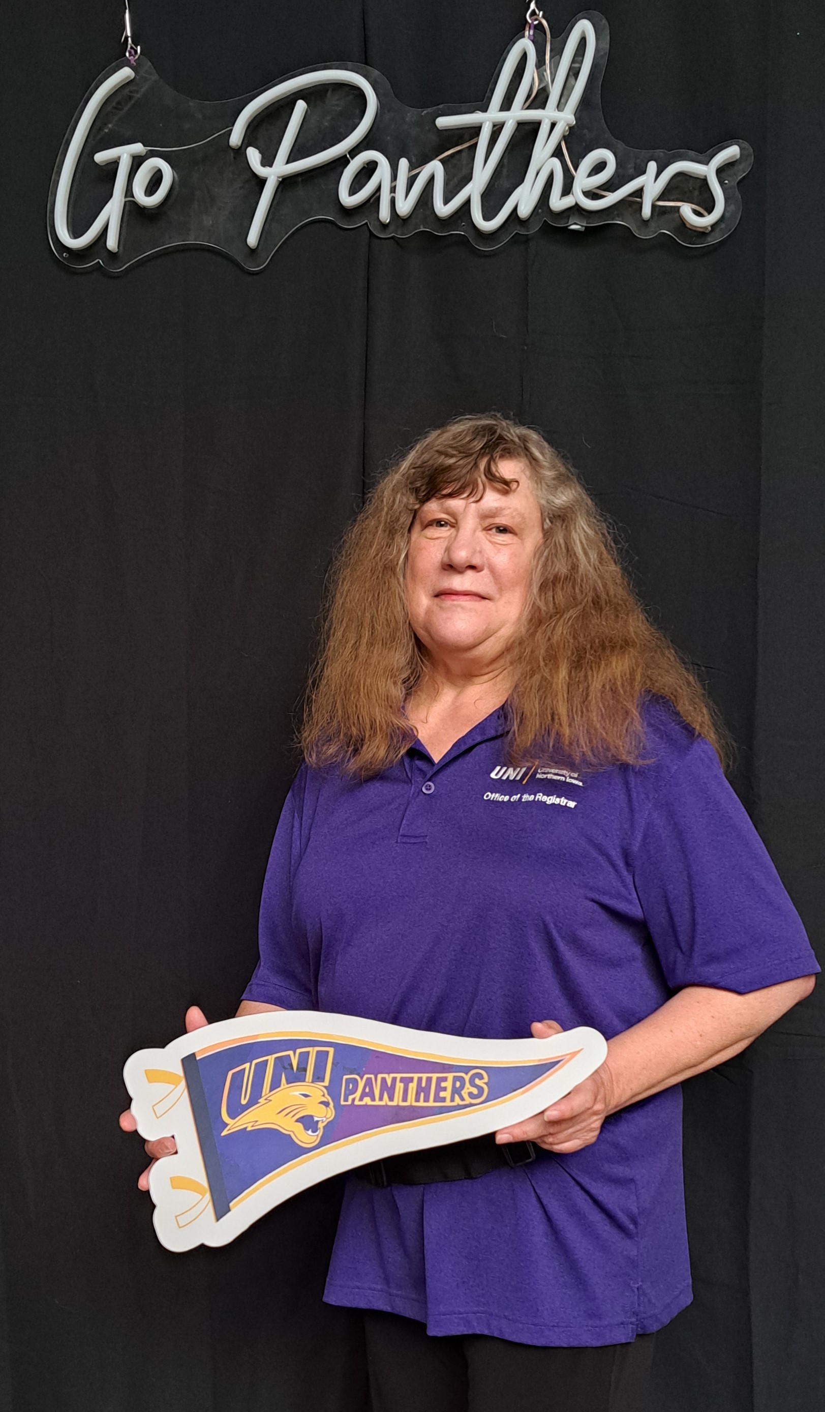 Janet holding a UNI pennant under a Go Panthers sign